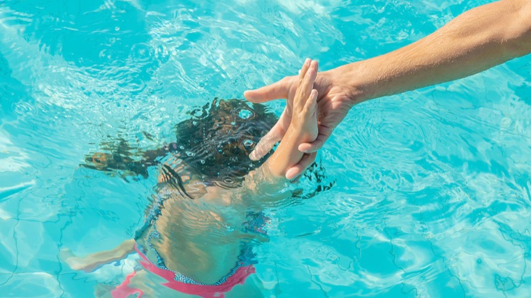 Un adulto tende la mano a un bambino sott'acqua in piscina